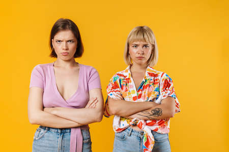 Portrait of two upset lovely girlfriends wearing summer clothes standing isolated over yellow backgroundの写真素材