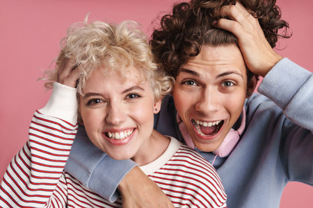 Happy young couple of teenagers standing isolated over pink background, wearing t-shirts, hugging,...