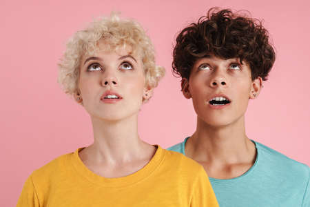 Portrait of an excited couple looking up into the distance isolated on pink backgroundの写真素材