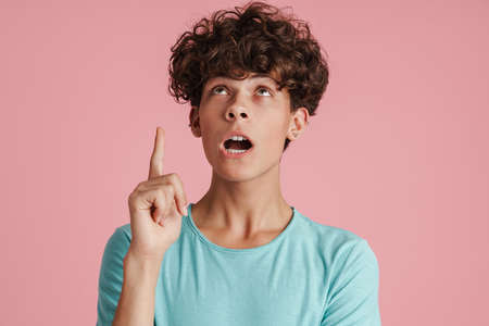 Young teenager pointing finger at copy space isolated over pink background