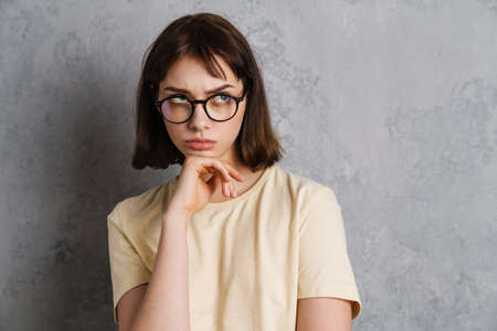 Attractive pensive thoughtful young woman standing isolated over gray background