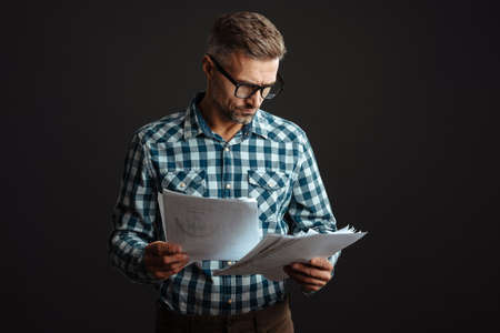 Image of a handsome serious grey-haired man holding documents isolated over grey wall backgroundの写真素材