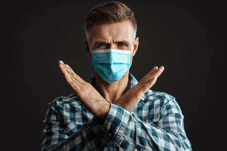 Photo of serious grey-haired man wearing face mask and showing stop gesture isolated over grey wall...