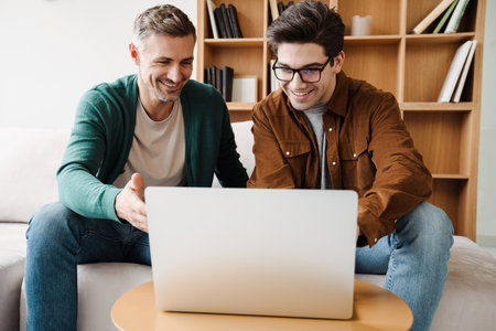 Happy young gay couple using laptop computer while sitting on a couch at homeの写真素材