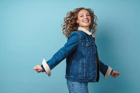 Blonde happy woman in denim jacket smiling while walking isolated over blue wallの写真素材