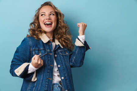Blonde excited woman laughing and making winner gesture isolated over blue wallの写真素材