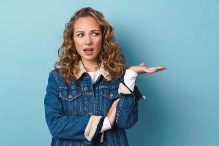 Blonde displeased woman frowning and holding copyspace isolated over blue wallの写真素材