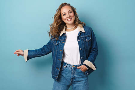 Blonde happy woman smiling and looking at camera isolated over blue wallの写真素材