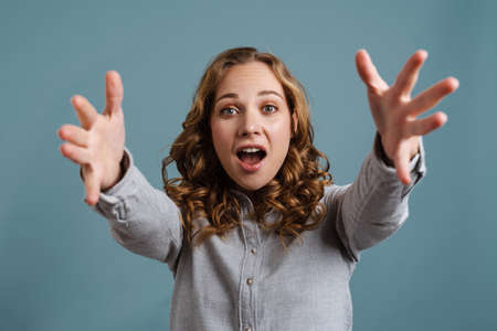 Surprised beautiful girl reaching out her hands at camera isolated over blue backgroundの写真素材