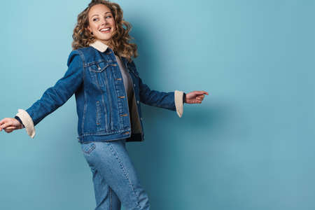 Blonde happy woman in denim jacket smiling while walking isolated over blue wallの写真素材