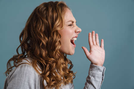Irritated beautiful blonde girl gesturing an screaming aside isolated over blue backgroundの写真素材
