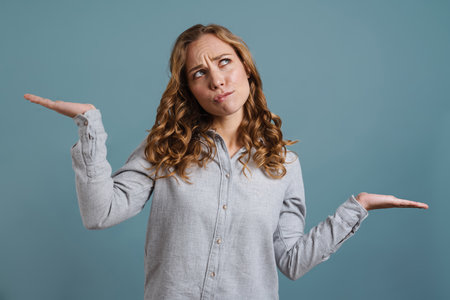 Portrait of a pretty confused woman shrugging shoulders isolated on a blue background