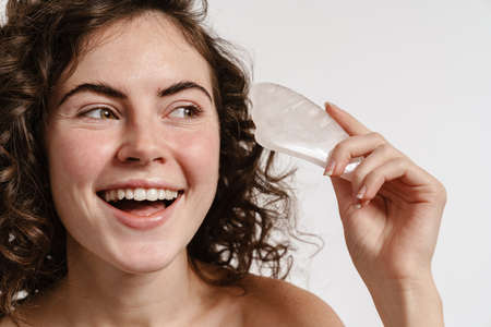 Happy shirtless girl smiling while posing with gua sha stone isolated over white background