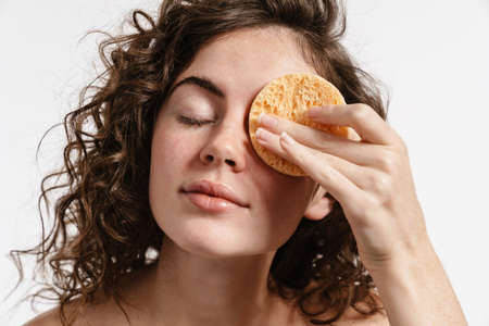 Beautiful shirtless curly girl using cosmetic sponge isolated over white background