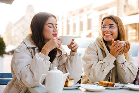 Two cheerful attractive women friends having tea and cakes at the cafe outdoorsの写真素材