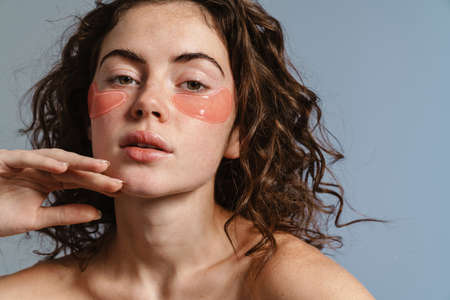 Beautiful shirtless girl with eyes patches posing at camera isolated over blue backgroundの写真素材