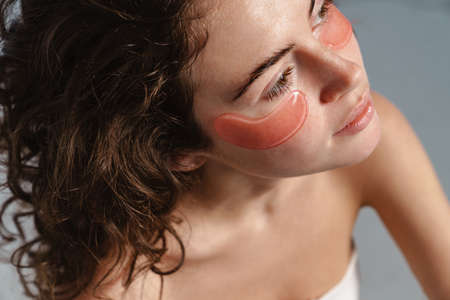 Beautiful half-naked nice girl posing with eye patches isolated over blue backgroundの写真素材