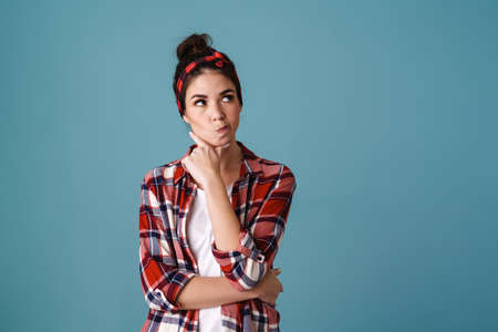 Puzzled beautiful brunette girl posing and looking aside isolated over blue backgroundの写真素材