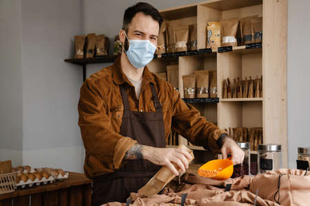 Happy mid aged farmer man in protective medical face mask packing grains at the organic produce...
