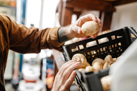 White bearded seller man holding mushroom while working in local eco shopの写真素材
