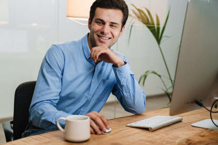 Smiling businessman sitting at office desk working on computerの写真素材