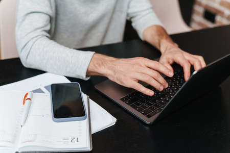Man hands typing on laptop over table with documents and mobile phone, close up