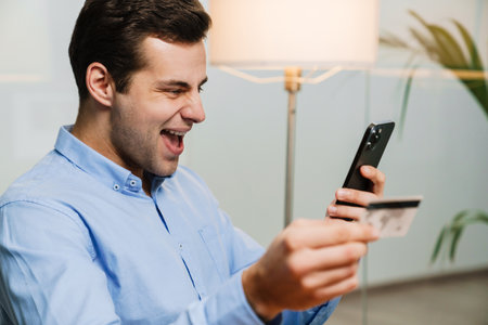 Happy office worker holding credit card and mobile phone, celebrating success
