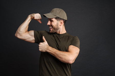 Strong healthy military man showing biceps isolated over black wall