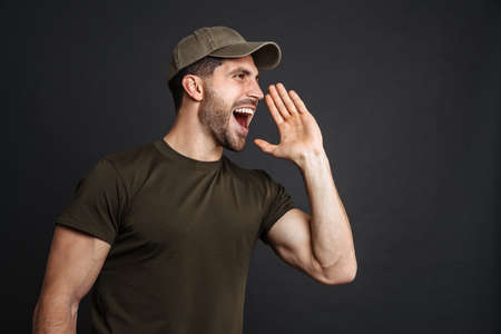 Excited military unshaven man screaming and looking aside isolated over black background