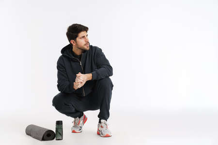 Young athletic sportsman posing with fitness mat and water bottle isolated over white background