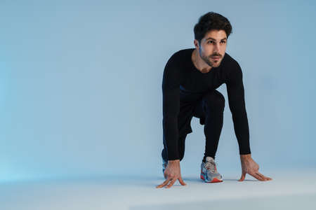 Young athletic sportsman doing exercise while working out isolated over blue background