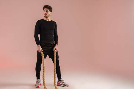 Handsome athletic sportsman posing with battle ropes isolated over pink backgroundの写真素材