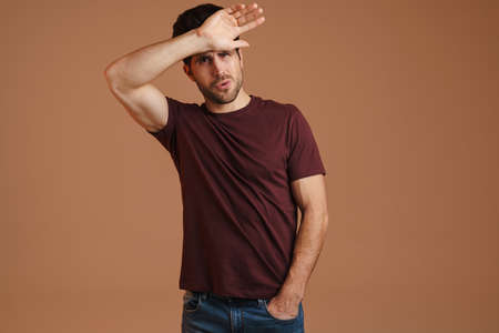 Displeased young man with headache touching his forehead isolated over beige background
