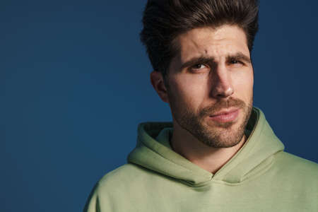 Perplexed handsome man in sportswear posing and looking at camera isolated over blue backgroundの写真素材