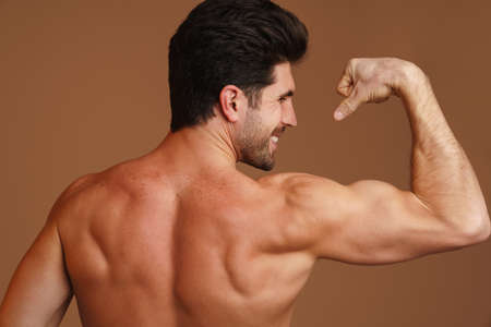 Shirtless happy man smiling and showing his biceps at camera isolated over beige backgroundの写真素材
