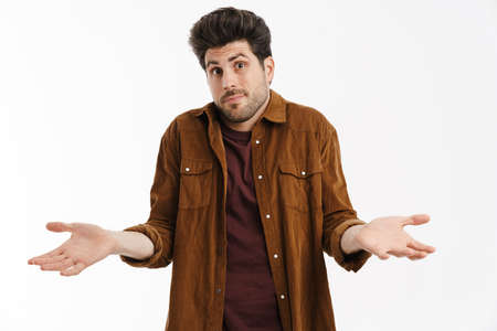 Perplexed young unshaven man showing and holding copyspace isolated over white background