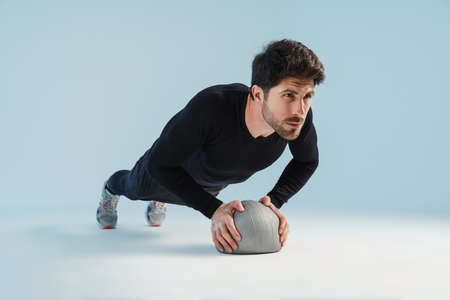 Handsome athletic sportsman working out with medicine ball isolated over blue background