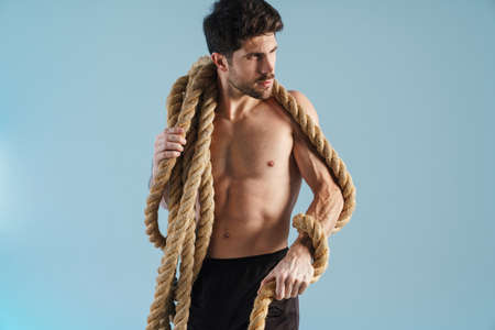 Shirtless athletic sportsman posing with battle ropes isolated over blue backgroundの写真素材