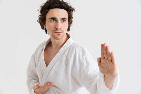 Young caucasian sportsman dressed in kimono practice in karate isolated over white background