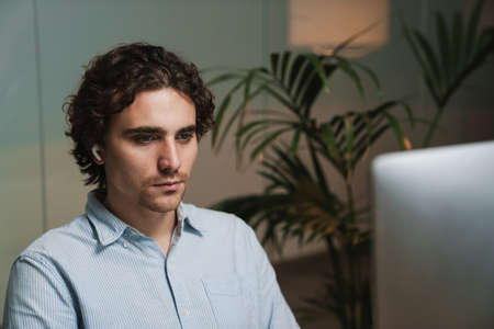 Caucasian young serious businessman in earphones working on computer in office