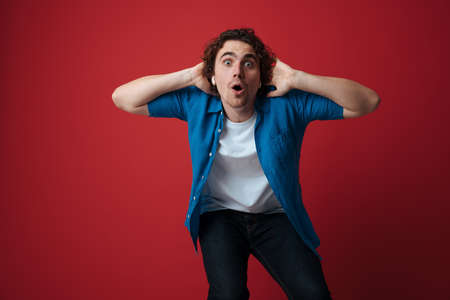 Amusing handsome man in earphones making fun on camera isolated over red backgroundの写真素材