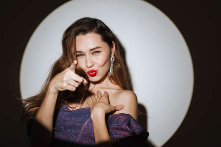 Happy beautiful girl looking and pointing finger at camera isolated over projector lightの写真素材