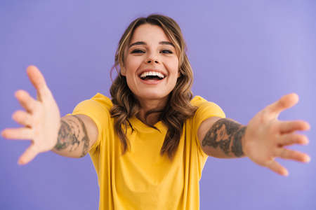 Happy beautiful girl laughing while reaching out her hands at camera isolated over purple backgroundの写真素材