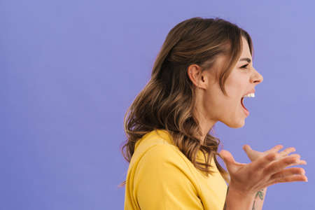 Angry caucasian girl screaming and looking aside isolated over purple background