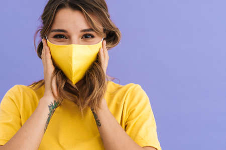 Portrait of a young happy woman wearing protective medical face mask isolated over blue background