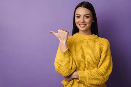Happy nice girl smiling while pointing finger aside isolated over purple backgroundの写真素材