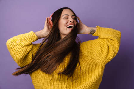 Happy young woman in headphones over violet wall background, listening to music, dancing