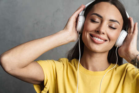 Close-up portrait of a happy young pretty girl relaxing in headphones isolated over gray backgroundの写真素材
