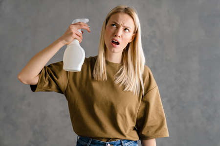 Displeased european woman posing with cleaning spray isolated over grey wallの写真素材