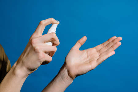 Closeup photo of hands and sanitizer spray isolated over blue wall